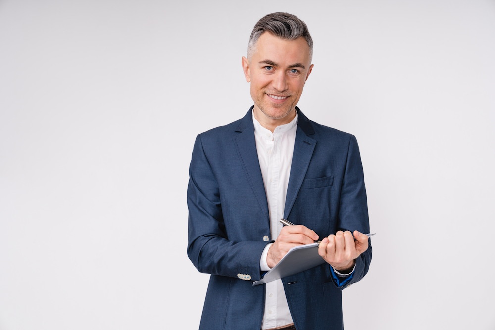 Confident mature businessman writing on clipboard isolated over white background